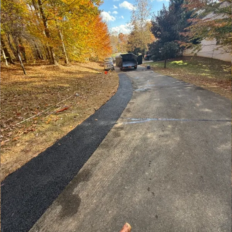 A driveway is being widened with a new strip of asphalt on one side.